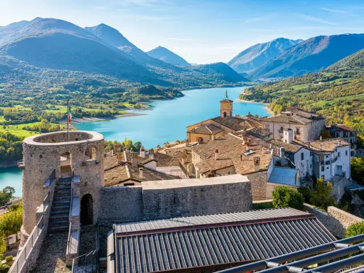 Borgo medievale con torre e lago turchese, incastonato tra i monti dell'Abruzzo.