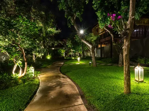 Un chemin sinueux traverse un jardin luxuriant illuminé par des lumières LED, créant une ambiance magique. La couleur LED met en valeur la végétation et l'architecture.