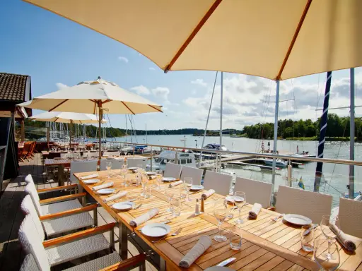 Väl dukade bord på en restaurang vid havet med segelbåtar i bakgrunden.