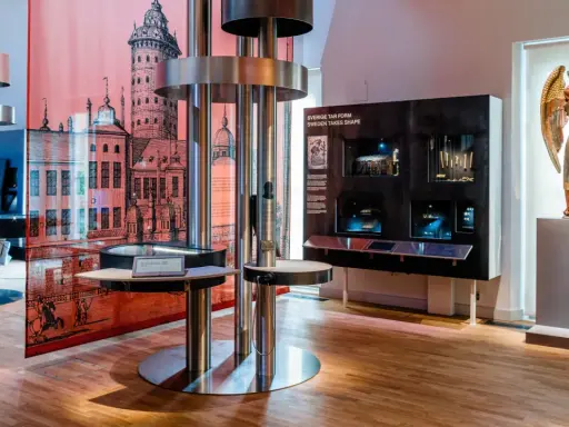 Utställning på ekonomiska museet med en stor illustration av en stad, en skulptur av en ängel och interaktiva displayer.