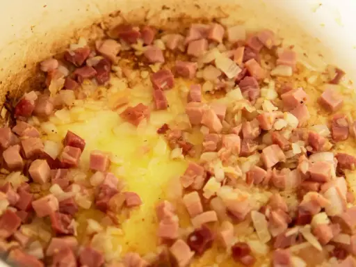 Guisantes con jamón y cebolla dorándose en una sartén con aceite. Un plato tradicional español.