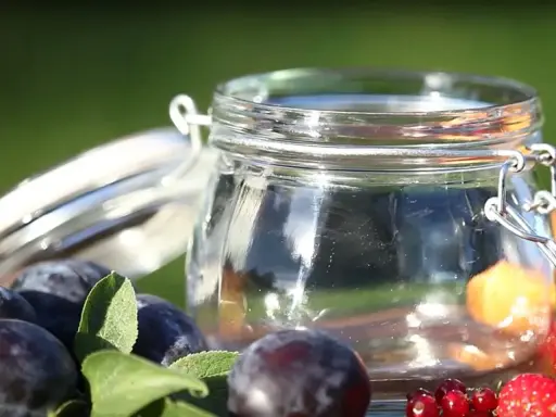 Ein Glas mit frischen Pflaumen und Beeren, bereit für Marmelade. Vorsicht bei der Zubereitung, um Botulismus zu vermeiden.