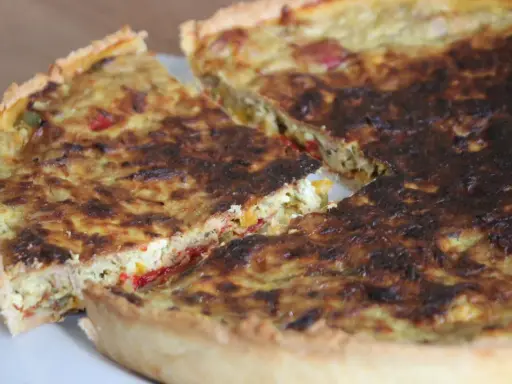 Une part de quiche poivron feta dorée, avec des morceaux de poivrons colorés et de feta crémeuse dans sa garniture.