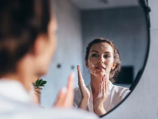 Une femme se regarde dans un miroir, appliquant de la mousse sur son visage pour un double nettoyage.
