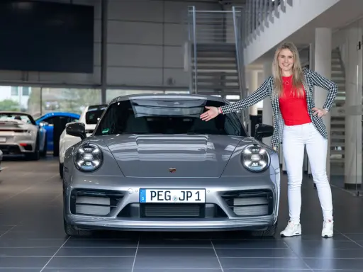 Eine Frau präsentiert stolz einen grauen Porsche Carrera T. Die Wertentwicklung dieses Sportwagens ist ein spannendes Thema für Enthusiasten.