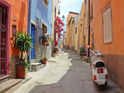 Un vicolo colorato con case arancioni e blu, fiori rossi e una Vespa bianca. Perfetto per le tue idee weekend nord Italia.