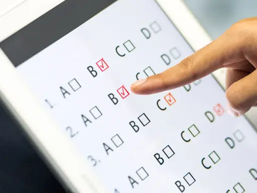Palec wskazuje odpowiedź B na ekranie tabletu, gdzie trwa test baltimorski. Zaznaczone są już odpowiedzi B i C.