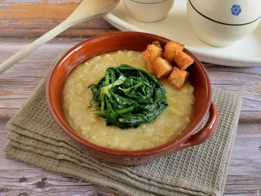 Piatto di fave e cicoria, una crema gialla con verdura verde al centro e crostini dorati.