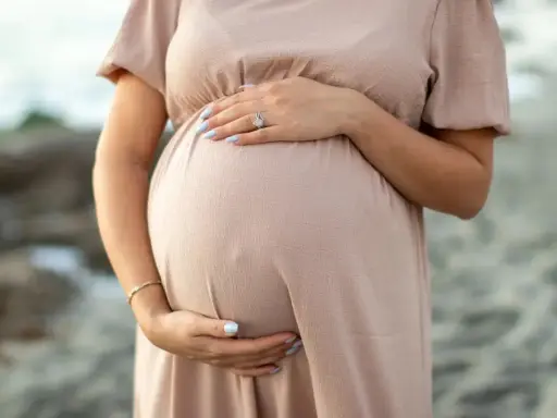Brzuch kobiety w ciąży, delikatnie otulony dłonią. W trosce o zdrowie maluszka, przyszła mama unika kosmetyków z retinolem.