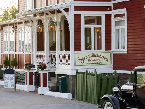 Strandflickornas Havshotell i Lysekil, en charmig röd byggnad med vita detaljer, välkomnar besökare. En klassisk bil står parkerad framför.