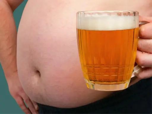Ein Bierbauch, der zeigt, dass Bier dick macht. Eine Hand hält ein Glas Bier vor dem Bauch.