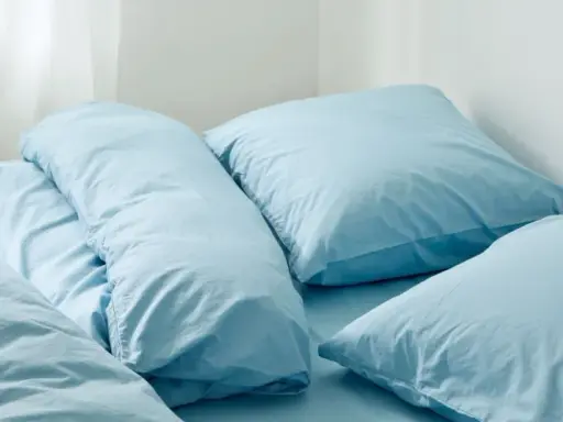 En bädd med ljusblå sängkläder, troligen percale eller satin, med flera kuddar och ett täcke.