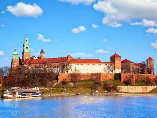 Zamek Królewski na Wawelu, z zielonymi wieżami i czerwonymi dachami, góruje nad Wisłą. Ciekawostki o jego historii czekają na odkrycie.