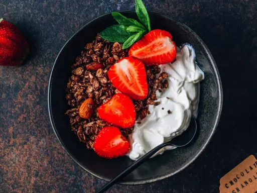 Schüssel mit Schokoladengranola, frischen Erdbeeren und cremigem Skyr oder Magerquark, garniert mit Minze.
