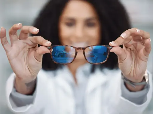 Kobieta w białym kitlu prezentuje okulary relaksacyjne z niebieskimi soczewkami, odbijającymi wnętrze sklepu.