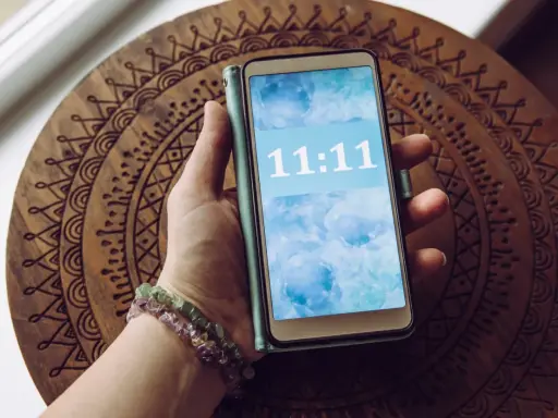 Dłoń trzyma telefon z wyświetloną godziną 11:11, co dla wielu ma szczególne znaczenie.