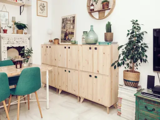 Muebles de madera clara con tiradores verdes, una mesa con sillas turquesas y una chimenea decorada. Inspiración para tu gama de colores para pintar muebles de madera.