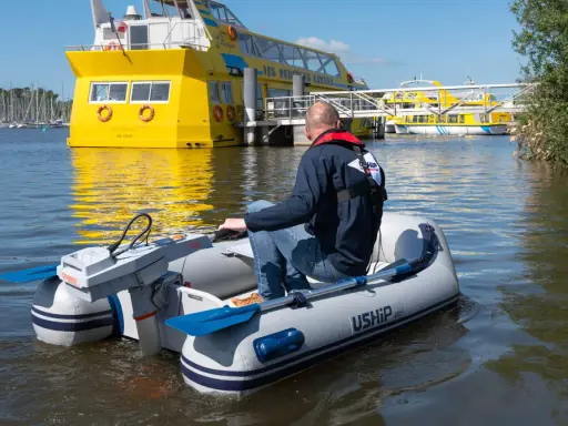 Un homme pilote un bateau gonflable propulsé par la puissance d'un moteur électrique, naviguant près d'un grand bateau jaune.