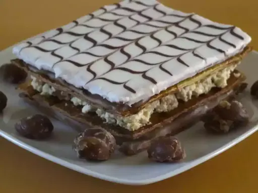 Un délicieux fondant millefeuille, garni de crème pâtissière et décoré de glaçage blanc et chocolat, est présenté sur une assiette avec quelques marrons glacés.