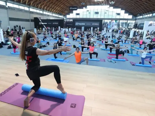 Allenamento di gruppo alla fiera dello sport Rimini, con istruttrice e partecipanti su tappetini.
