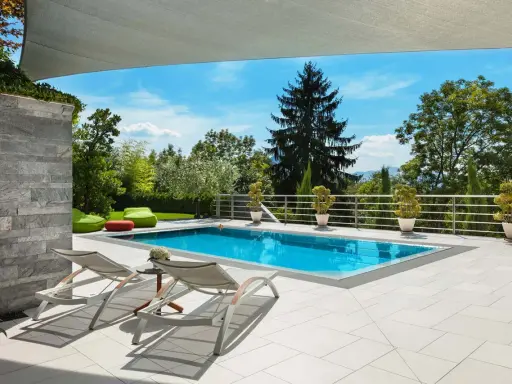 Moderne idee aiuole bordo piscina: piante in vaso e pouf colorati creano un'oasi rilassante.