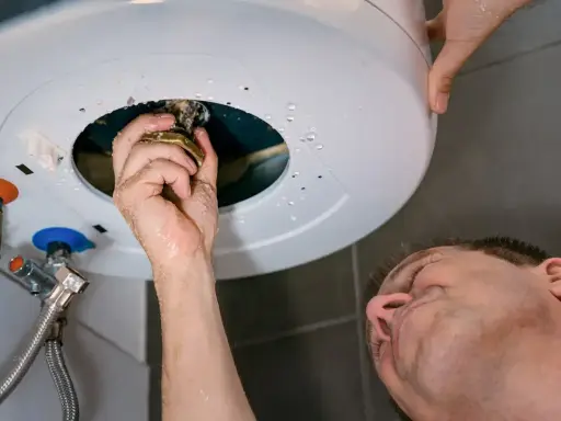 Main qui répare un chauffe-eau, une fuite d'eau s'échappe du cumulus qui fuit par le haut.