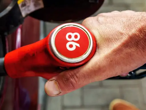 Mano sujetando una boquilla de gasolina roja con el número 96, indicando uno de los tipos de gasolina en España.