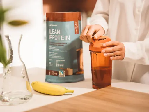 Eine Person bereitet einen Proteinshake zu. Die Packung "Lean Protein" zeigt 17g Protein pro Portion. Die Frage "wie viel protein pulver auf 500 ml" wird durch die Zubereitung beantwortet.