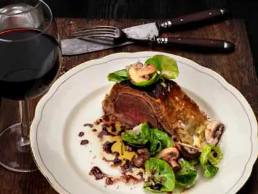 En saftig wellington biff serveras med svamp och grönsaker, ackompanjerad av ett glas rött vin.