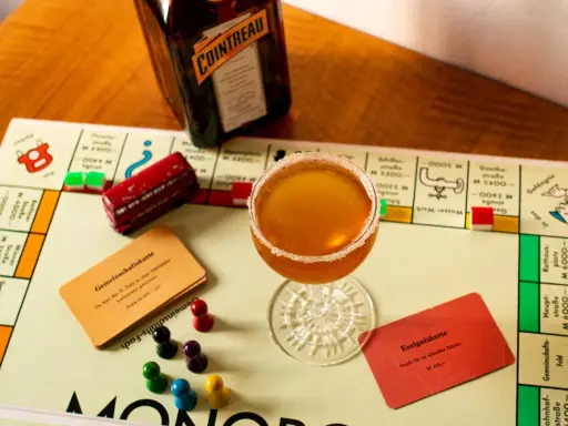 Ein Sidecar Cocktail steht auf einem Monopoly-Spielbrett neben einer Flasche Cointreau.