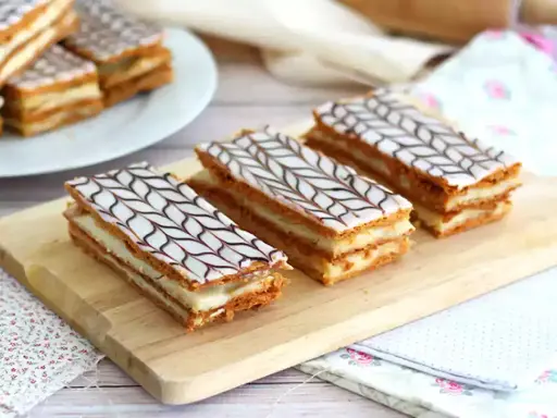 Tre läckra millefeuille-bakelser med lager av smördeg och kräm, toppade med vit glasyr och chokladmönster.