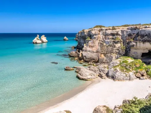 Scogliere calcaree e mare cristallino a Torre dell'Orso centro, con faraglioni che emergono dall'acqua turchese.
