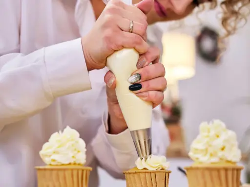 Une pâtissière décore des cupcakes avec une chantilly mascarpone aérienne.