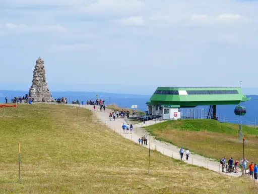 Feldberg: Steinkegel-Denkmal und Seilbahnstation mit Wanderern auf einem grasbewachsenen Hügel.