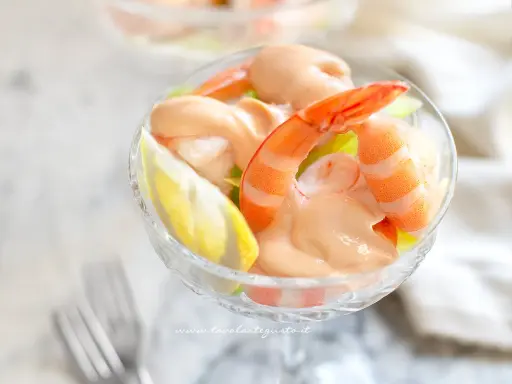 Un delizioso cocktail di gamberi servito in una coppa di cristallo, con una fetta di limone e una salsa rosa cremosa.