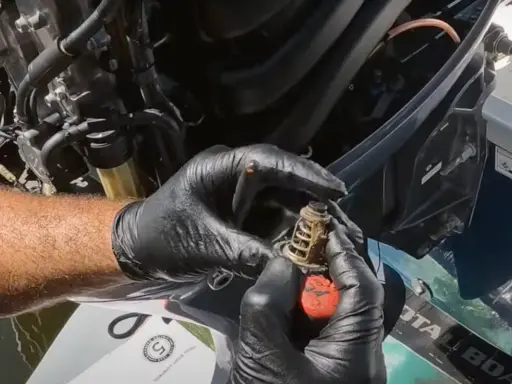 Mains gantées tenant un thermostat usagé, prêt pour le changement sur un moteur hors bord Yamaha.