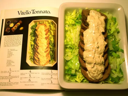 Vitello tonnato recept: skivad kalv med tonfisksås och sallad, bredvid en öppen kokbok med recept.