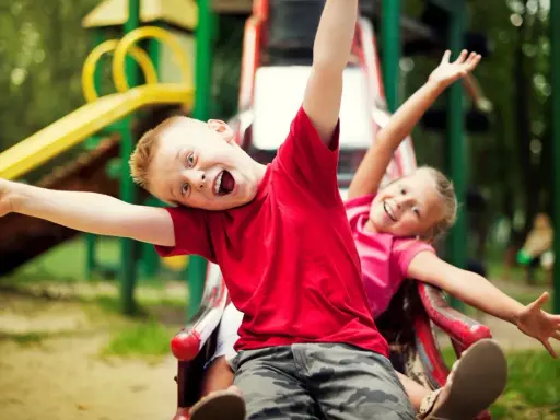 Bambino che salta sempre, con un sorriso contagioso, scende dallo scivolo con la sorella.