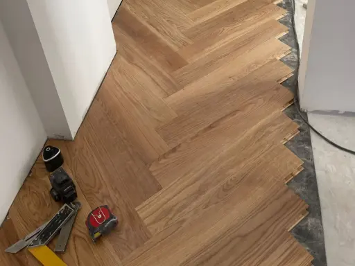 Instalación de suelo de madera en espiga. El rodapié igual que el suelo crea un acabado moderno y continuo. Herramientas de instalación a la vista.