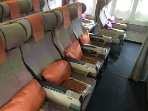 Fotele w samolocie linii lotniczych Emirates, z pomarańczowymi poduszkami i zagłówkami, gotowe na podróż.
