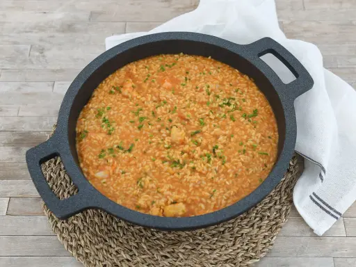 Arroz cremoso con gambones, adornado con cebollino fresco, servido en una paellera sobre una mesa de madera.