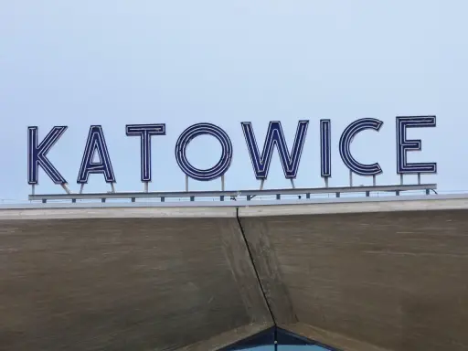 Napis "KATOWICE" z niebieskimi neonami na tle nieba, nad betonową konstrukcją.