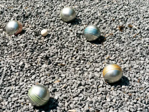 Boules de pétanque argentées, certaines rayées de couleurs vives, reposent sur un lit de gravier gris. Le jeu de pétanque est prêt à commencer.