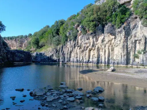 Un'oasi naturale nella Tuscia: un fiume serpeggia tra imponenti pareti rocciose ricoperte di vegetazione, creando uno scenario suggestivo.