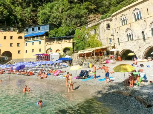 Ein idyllischer **Geheimtipp Italien Strand** mit bunten Sonnenschirmen, sonnenbadenden Menschen und kristallklarem Wasser vor malerischer Kulisse.