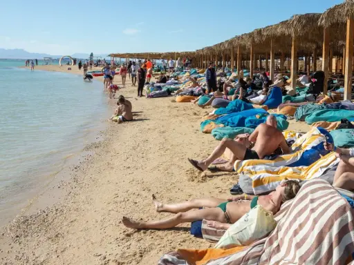 Słoneczna plaża w Egipcie w maju. Ludzie odpoczywają na leżakach pod palmowymi parasolami, ciesząc się piękną pogodą.