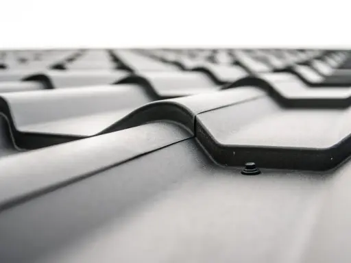Detaljerad vy av ett tak med svarta, profilerade plåtar. En skruv syns i förgrunden, redo att fästa plåten. Perfekt för att måla galvad plåt.