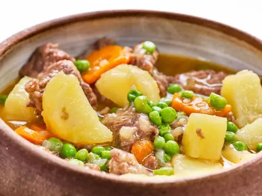 Un reconfortante ragout de ternera con patatas, zanahorias y guisantes en un cuenco rústico.