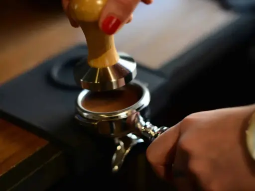 Barista tamped den gemahlenen Kaffee für einen perfekten Espresso. Die Espresso-Definition beginnt hier.