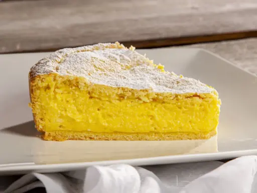 Una fetta di crostata di ricotta, con la sua base dorata e il ripieno cremoso, spolverata di zucchero a velo.